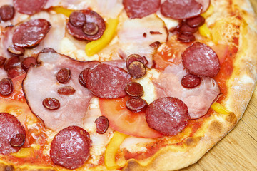 Crispy salami pizza with vegetables, close up. Juicy pizza with spicy sausages, cheese, tomatoes and bell pepper.