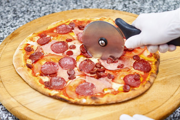 Pizza cutting using wheel cutter. Hand cutting pizza using round tool.