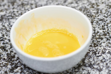 White bowl with beaten eggs. Close up beaten yolks in bowl on table.