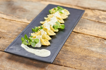 Row of ravioli on black rectangle plate. Decorated ravioli dish.