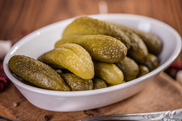 green pickled marinated gherkins in a white dish on wood table