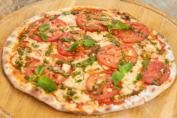 Top view tomato pizza with greens on wooden board. Appetizing cooked tomato pizza with basil.