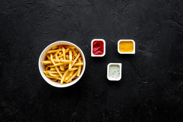 French fries with sauces on black background top view copy space