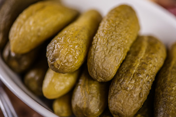 green pickled marinated gherkins in a white dish on wood table