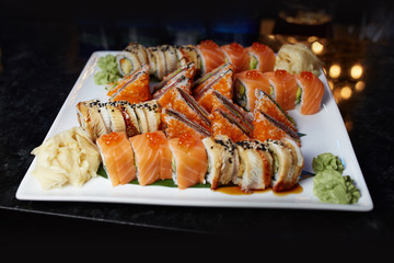 Eating sushi rolls. Japanese food restaurant, sushi maki gunkan roll plate or platter set. Closeup of hand with chopsticks taking roll. Ginger, soy, wasabi. Sushi at black rustic wood background.