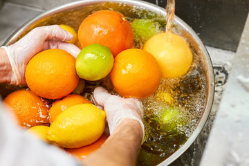 Chef washing mix of citrus fruits in a sink. Tap water overflowing metal basin with citrus fruits....