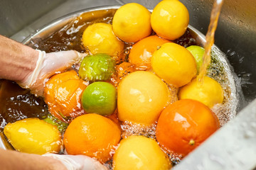 Plenty of citrus fruits in a metal bowl full of water under tap water.