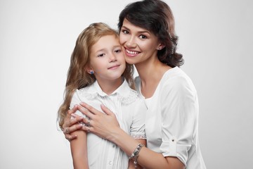 Close-up of wonderful family couple: beatiful mother and her little nice daughter. They are very happy with pretty smiles. They wear white t-shirts. Photo was made on the white studio background.