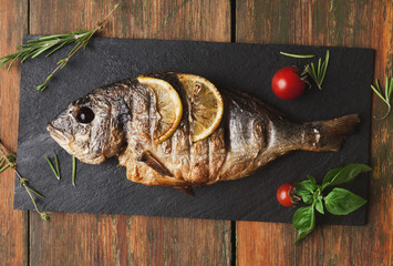 Whole grilled dorado with lemon slices on wood