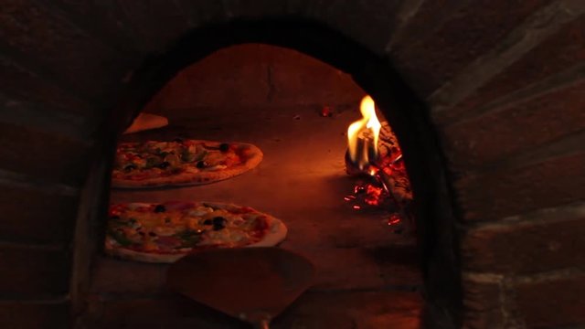 baking traditional italian pizza in a wood fired stone oven. pizzaiolo is using a pizza peel.