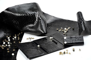 Glancy black leather pieces lay near woman s wallet with many sectors. They look like reptile skin....