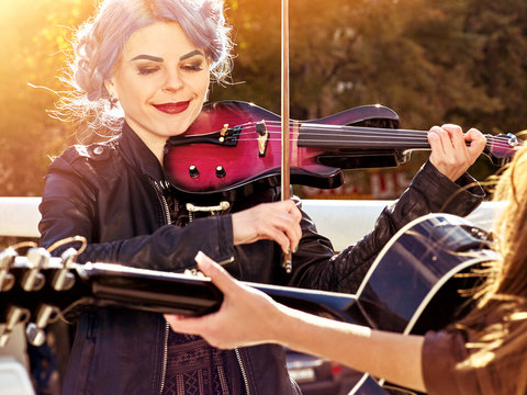 Music on violin by woman perform in park outdoor. Girl performing jazz on city street. Color tone on shiny sunlight background. Spring outside with blue hairstyle background. Toning of spring photo.
