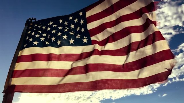 Tattered old American flag flying in the setting sunlight in slow motion against bright blue sky