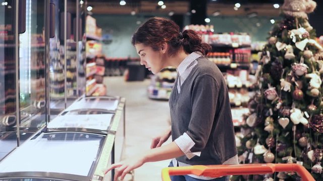 Young brunette girl takes a pack of butter from the freezer. Shopping at local grocery store