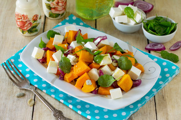 Warm pumpkin salad with onions, served with feta cheese, arugula and pumpkin seeds on a rustic table. The concept of healthy eating.