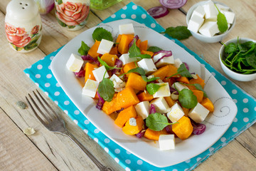 Warm pumpkin salad with onions, served with feta cheese, arugula and pumpkin seeds on a rustic table. The concept of healthy eating.