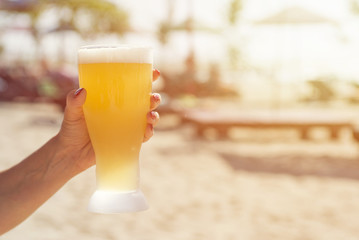 Hand of a man holding a glass of beer on the beach