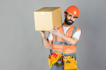 A man-builder in an orange helmet with a cardboard box in his hands. On a gray background