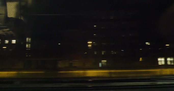 POV from Oresundstag fast train through window at houses, apartment buildings, industries factories and empty street at night - commuting by train in Denmark