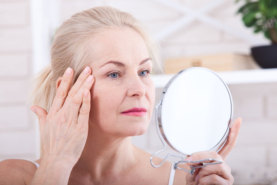 Middle aged woman looking at wrinkles in mirror. Plastic surgery and collagen injections. Makeup. Macro face. Selective focus