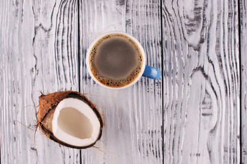 A cup of black coffee and a coconut on a wooden background