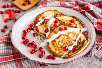 Pancakes with sour cream and pomegranate seeds on a plate.