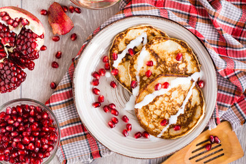 Pancakes with sour cream and pomegranate seeds on a plate. Top view