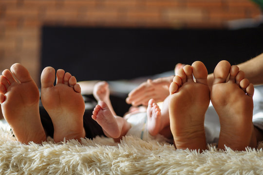 family laying on bed, their feets on focus. Mother, father and infant newborn baby son