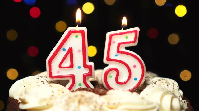 Number 45 on top of cake - forty five birthday candle burning - blow out at the end. Color blurred background