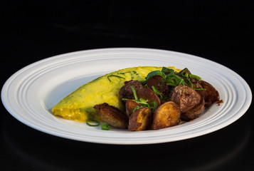 French omelet with crispy home fries and green onions on a white plate.