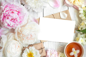 blank greeting card in frame made of peony, rose and jasmine flowers with cup of tea