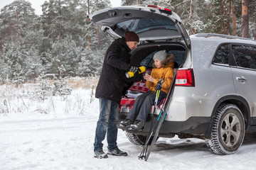 Father pouring hot drink for child after sports activities such as ski. Sitting back trunk of suv at winter season. Copyspace