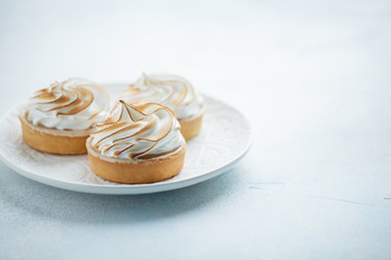 Delicious lemon tartlets with meringue on a white vintage plate. Sweet treat on a light blue background. copy space