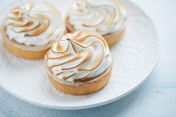 Delicious lemon tartlets with meringue on a white vintage plate. Sweet treat on a light blue background