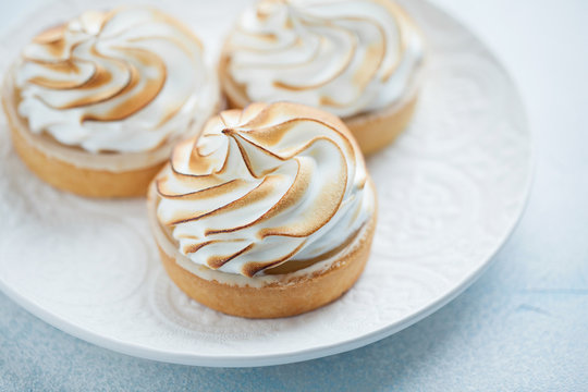 Delicious lemon tartlets with meringue on a white vintage plate. Sweet treat on a light blue background