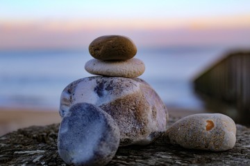 Stacked pebbles, balanced on a wooden groyne, with a sunset seascape in the background 