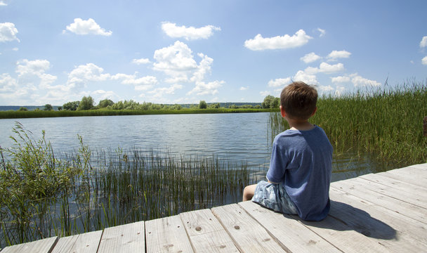 Boy Sitting On Pier Near Lake