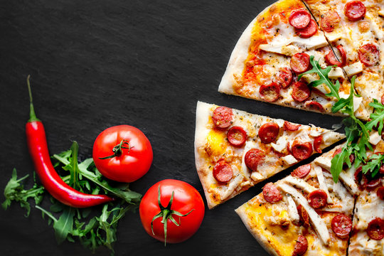 Meat  Pizza with sausage,  mozzarella cheese and tomato on black stone background with copy space. Pizza delivery.