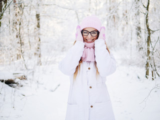 Adorable happy young blonde woman in pink knitted hat scarf having fun strolling snowy winter forest in nature