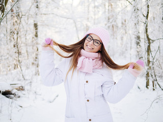 Adorable happy young blonde woman in pink knitted hat scarf having fun strolling snowy winter forest in nature
