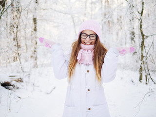 Fototapeta na wymiar Adorable happy young blonde woman in pink knitted hat scarf having fun strolling snowy winter forest in nature