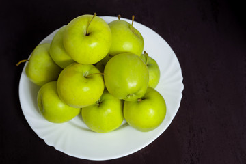 Green apples on a plate on a black textural background.