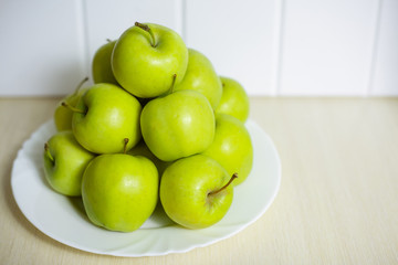 Green apples on a plate on a wooden table.