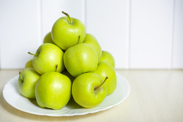Green apples on a plate on a wooden table.