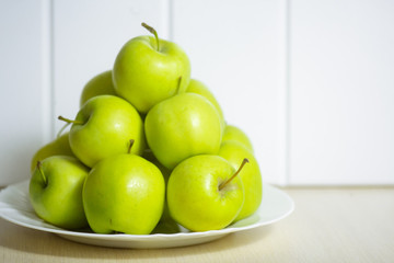 Green apples on a plate on a wooden table.