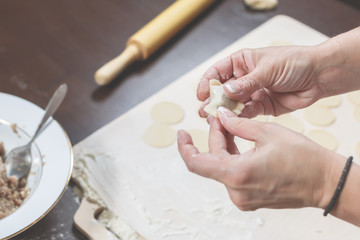 Fototapeta na wymiar Female hands mold homemade dumplings on the background of a wooden table