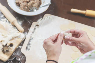 Female hands mold homemade dumplings on the background of a wooden table