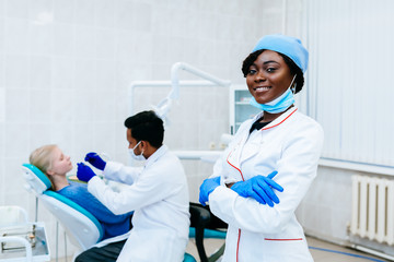 Young smiling African american female dentist in front of dentist checking teeth to patient at clinic. Dental clinic concept.