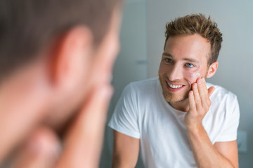 Handsome young man putting facial treatment face cream on clean skin in the morning after wash for skin moisturizing care. Dry skin problem. Men beauty routine.