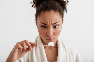 Close up of young neat girl looking at toothpaste with confused face. Isolated on background